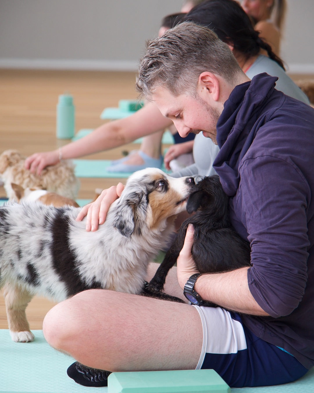 Man enjoying Puppy Yoga on the Central Coast, cuddling and bonding with playful puppies during a relaxing yoga class.