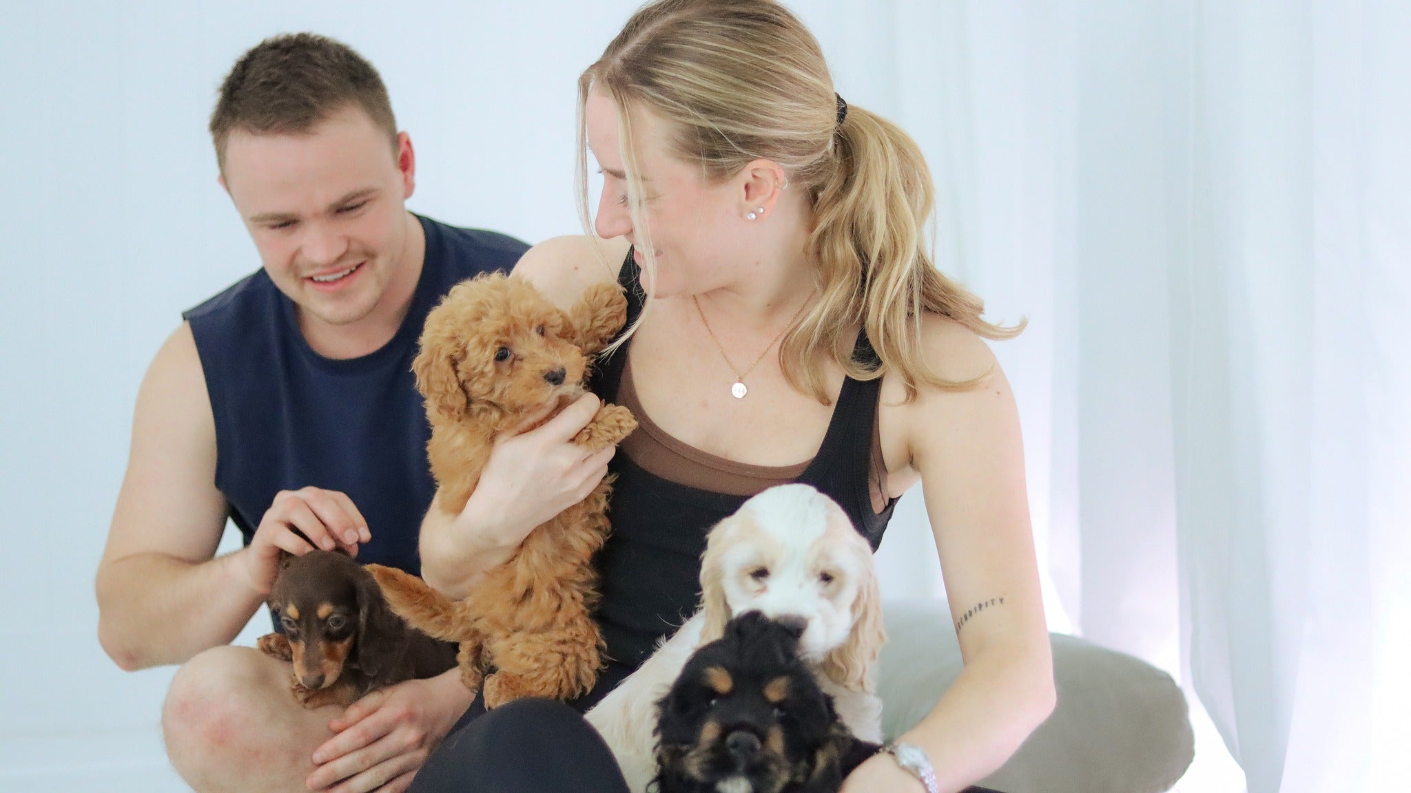 Two Puppy Yoga participants in Australia smiling and holding several puppies during a class, creating a joyful experience